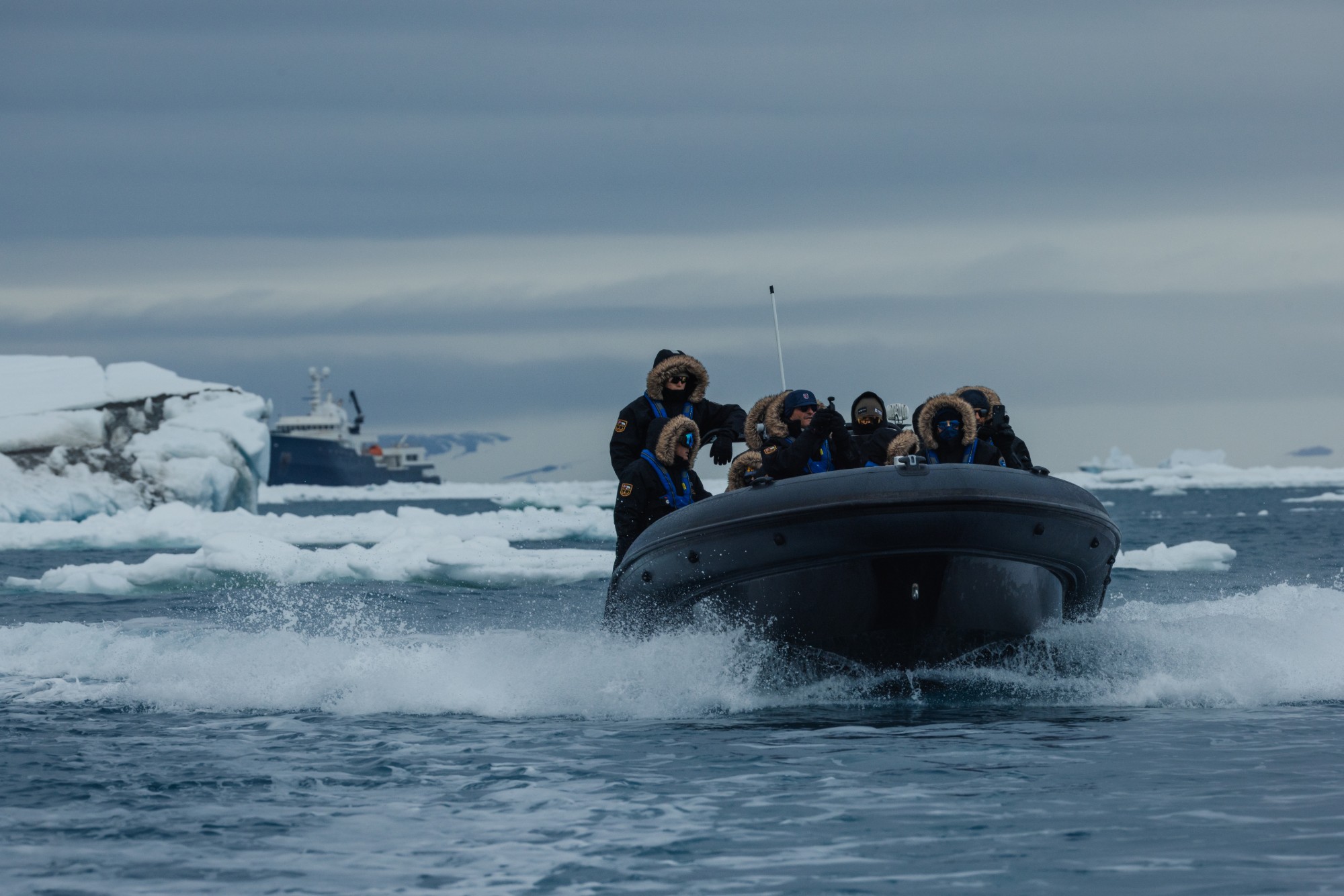 Expedition guests in a Zodiac speeding through Arctic pack ice, with their ship anchored beyond