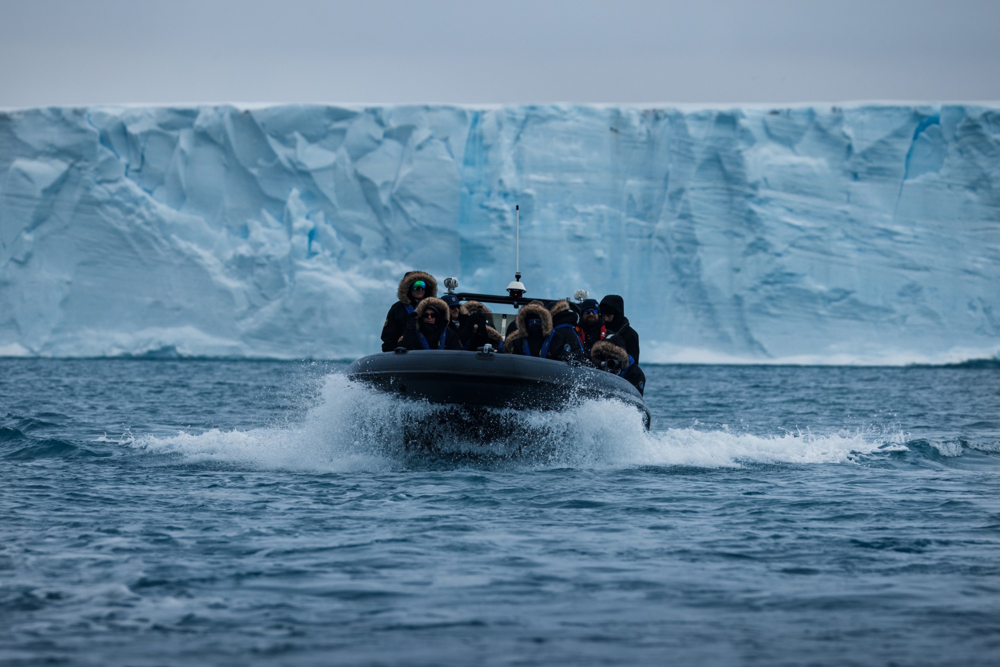 Guests in a Zodiac cruising beneath a towering wall of glacier ice