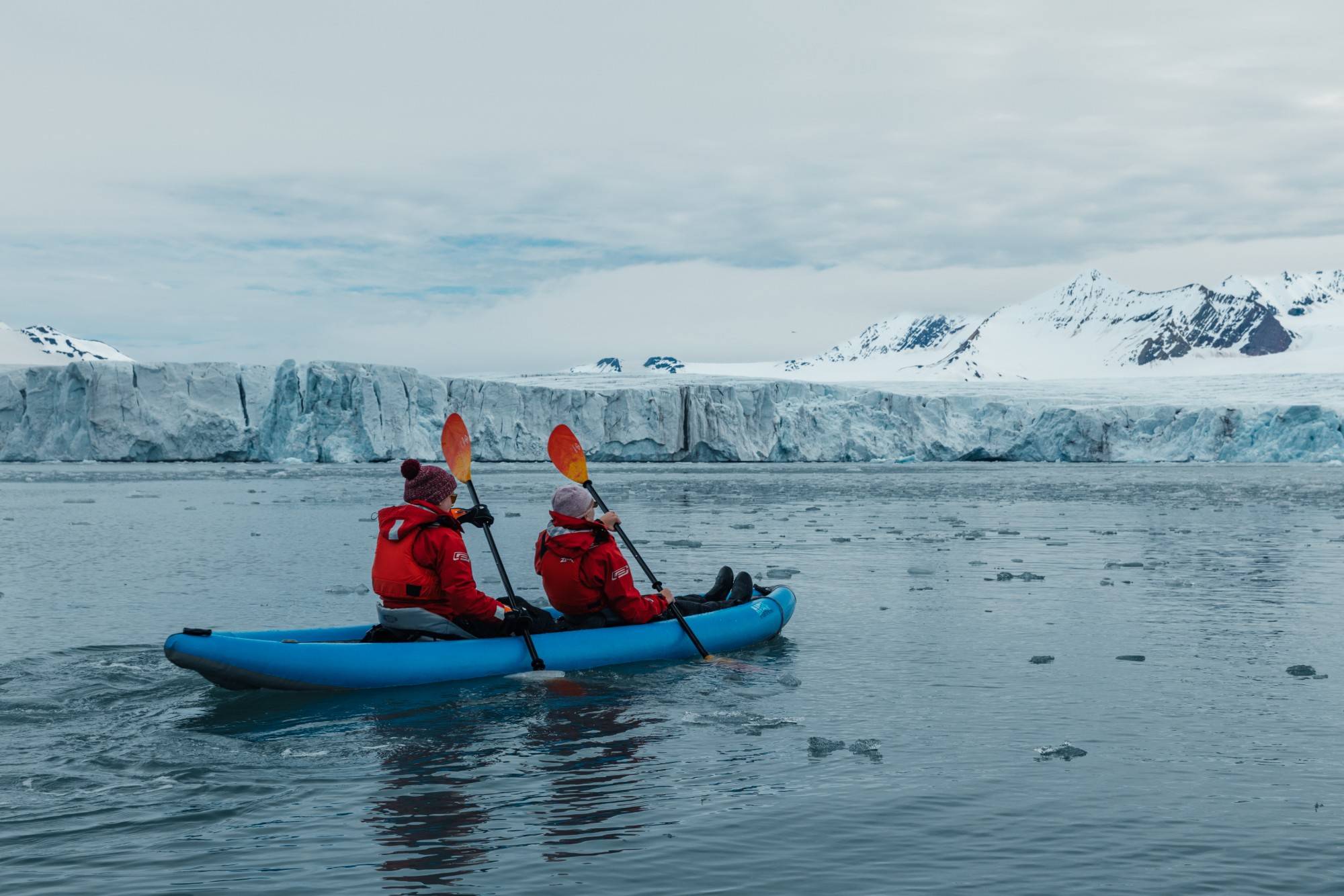 Two kayakers paddling among floating ice in front of a glacier front