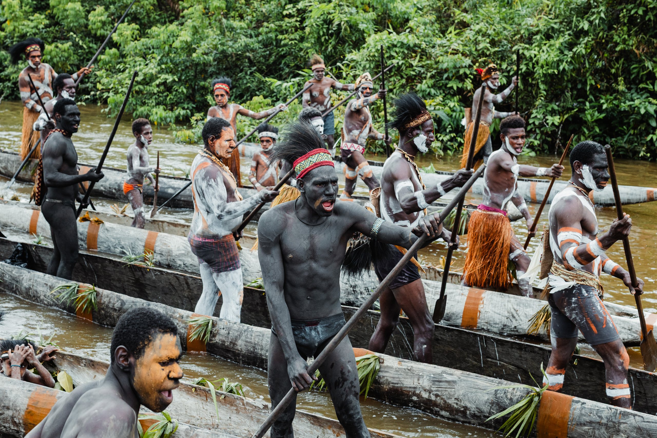 Asmat warriors paddling traditional canoes along a river