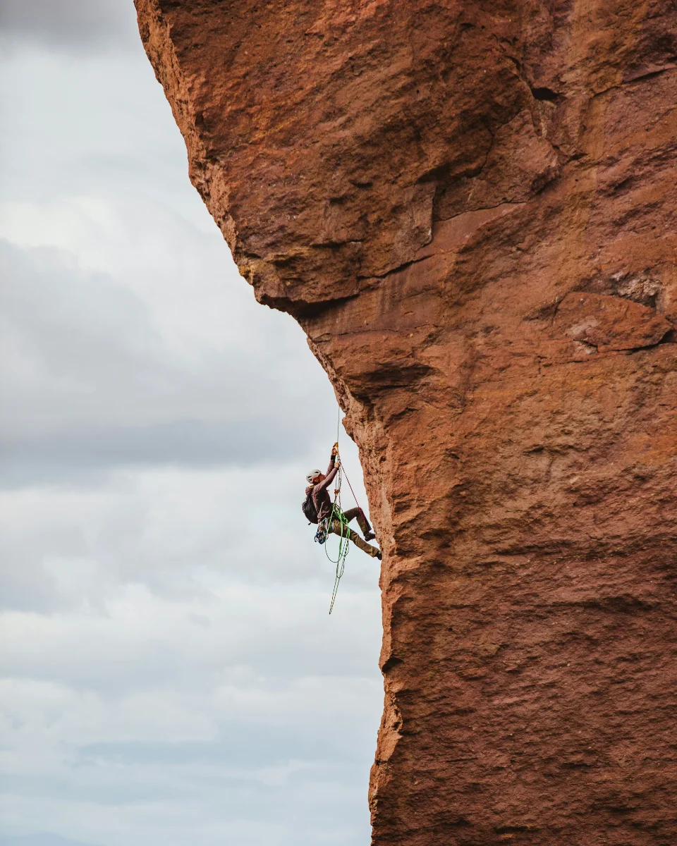 A rock climber on a rope, partway up an overhanging red cliff