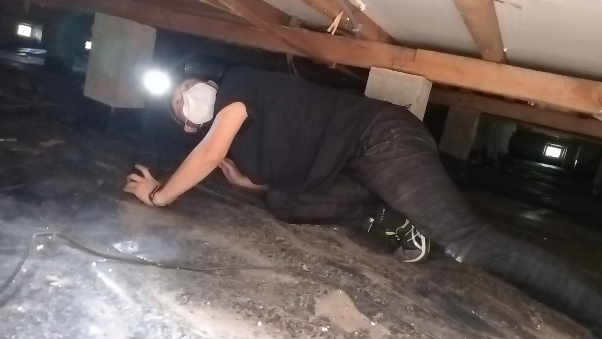 Frank crawling under a house with a head torch to check the subfloor during a building inspection