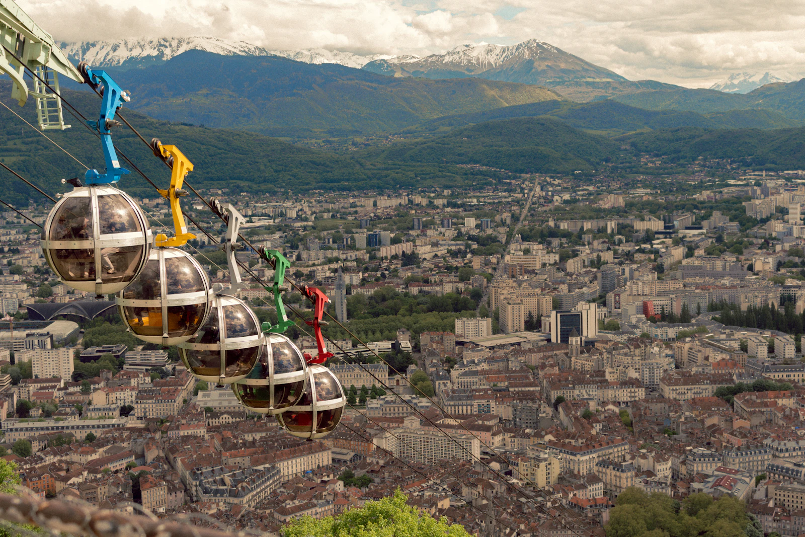 Cabines colorées du téléphérique de la Bastille au-dessus des toits de Grenoble, face aux montagnes enneigées