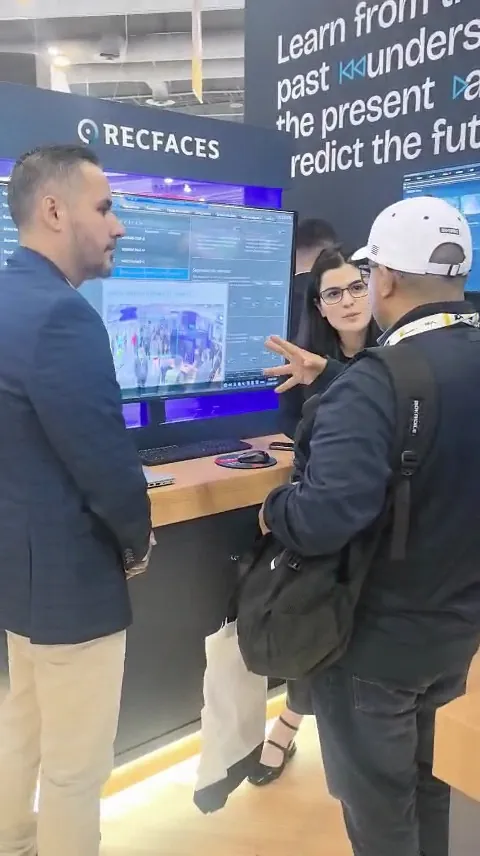 A RecFaces team member points at the demo screen while two visitors look on