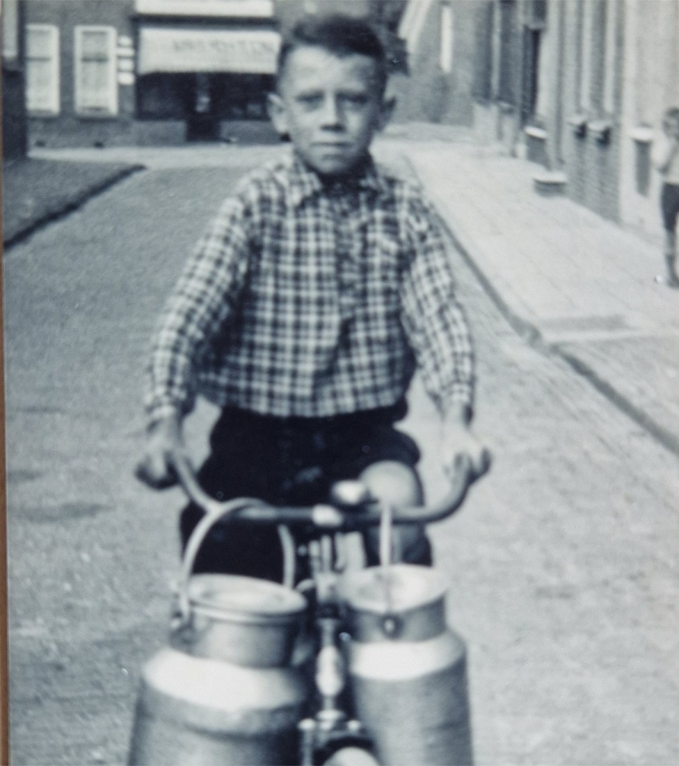 Oude zwart-witfoto van een jongen op een fiets met melkbussen — de overgrootvader achter de naam Bring the milk