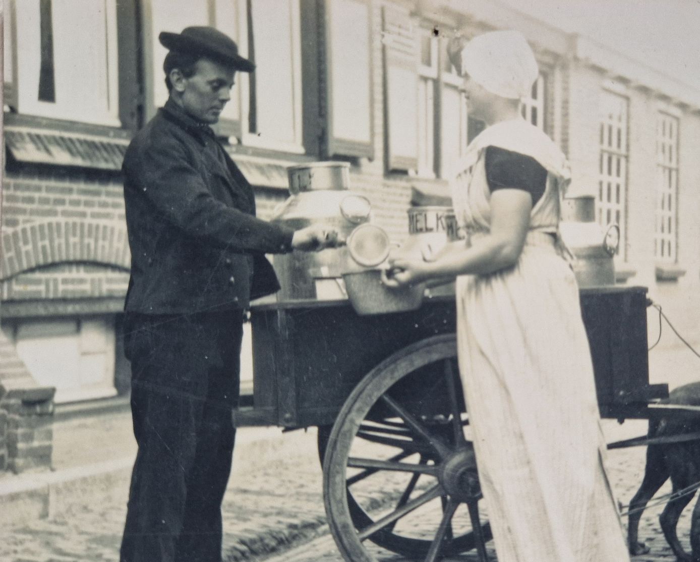 Oude zwart-witfoto van een melkboer die melk schenkt aan een vrouw bij de deur