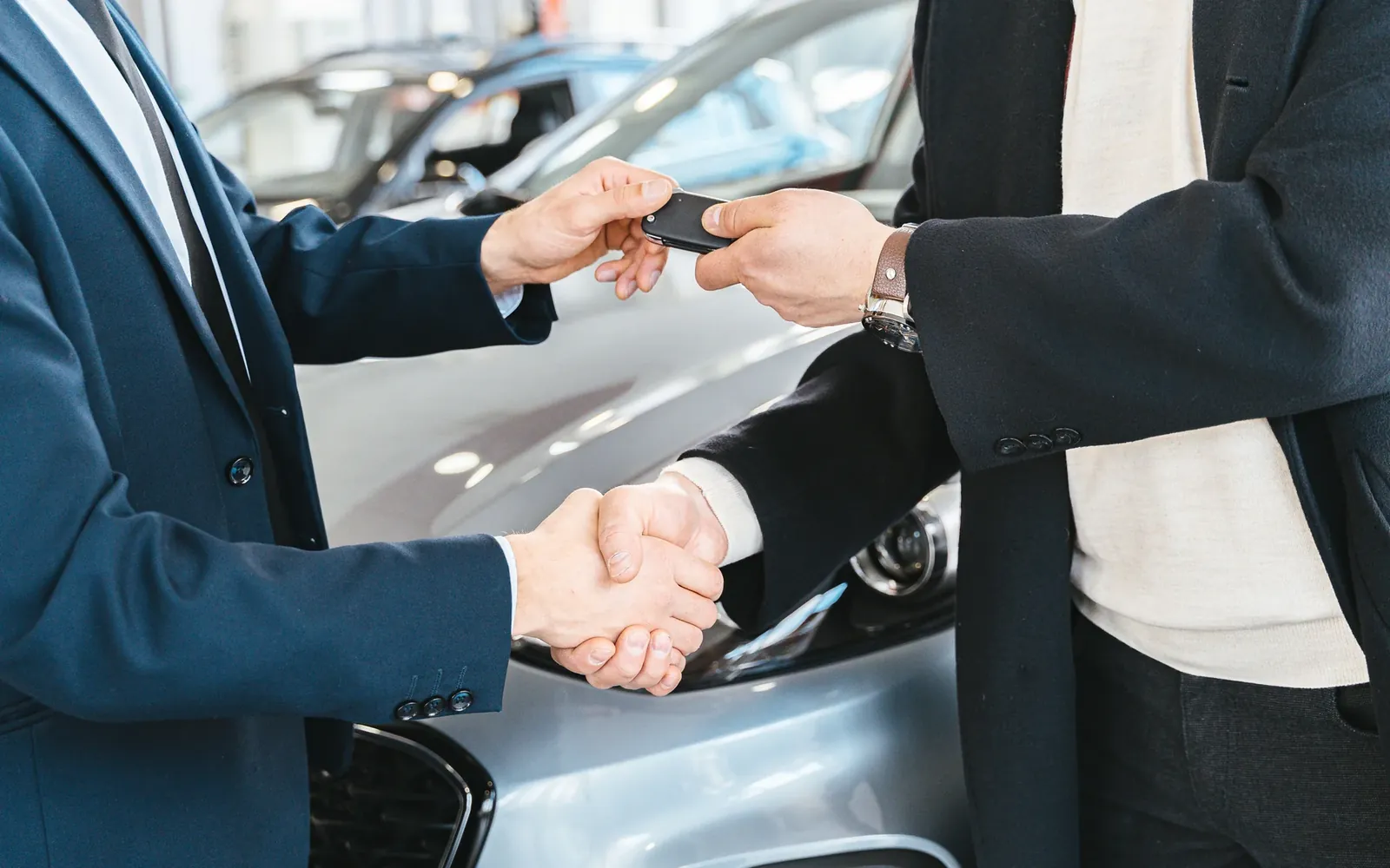 Two people shaking hands as car keys are handed over in a showroom