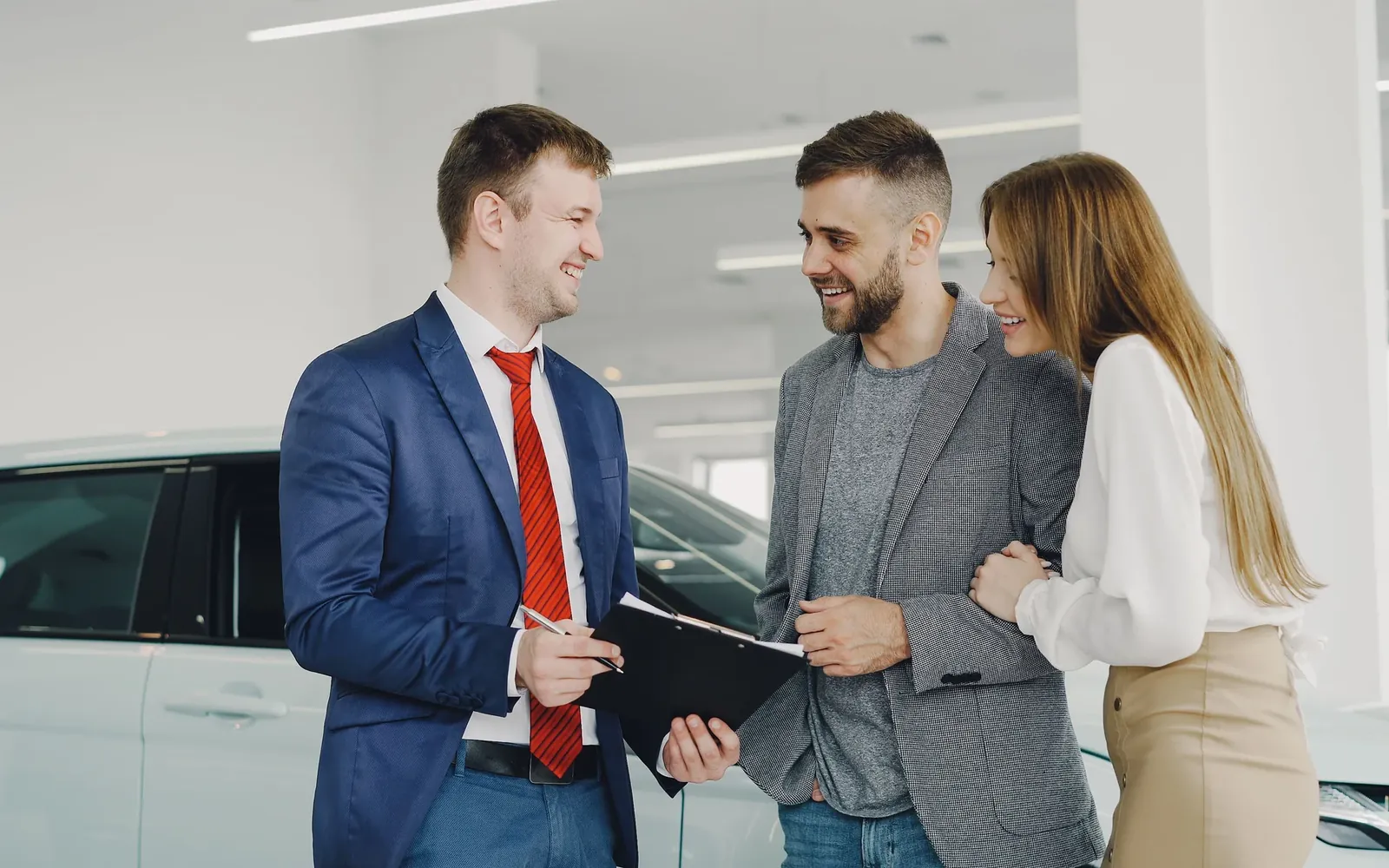 A salesperson talking a couple through paperwork beside a white car in a showroom