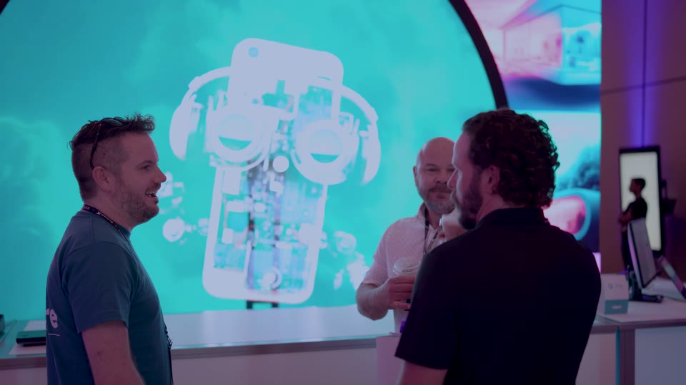 Attendees talking beside a HOLOFAN holographic display at the iQmetrix Summit X 2025 booth
