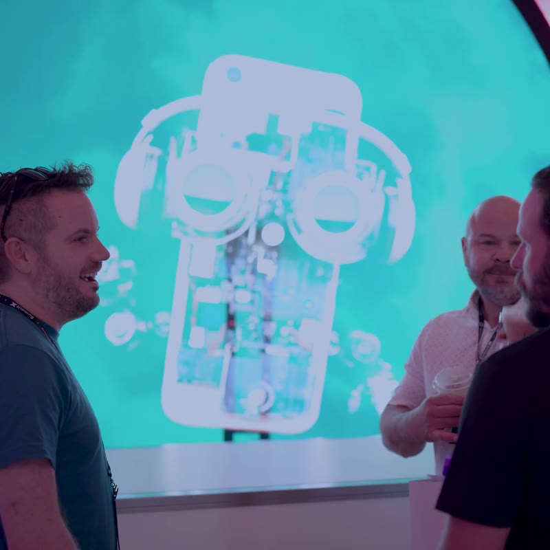 Attendees talking beside a HOLOFAN holographic display at the iQmetrix Summit X 2025 booth