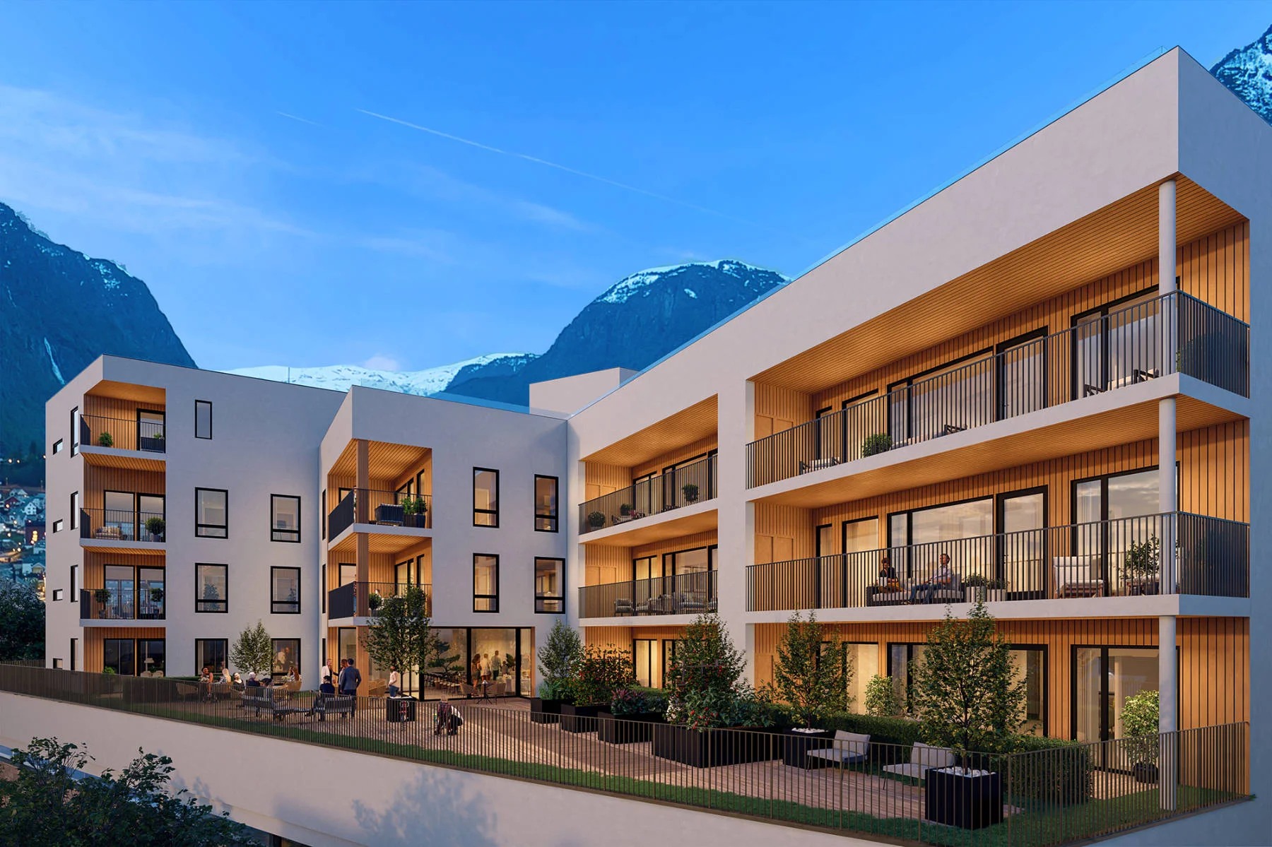 Moderne fasade med lyse flater og varme trebalkonger i kveldslys. Domus Gaarden ligger vakkert til mellom fjell og fjord.
