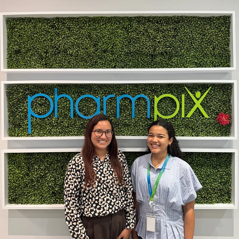 Two employees posing in front of the PharmPix office sign