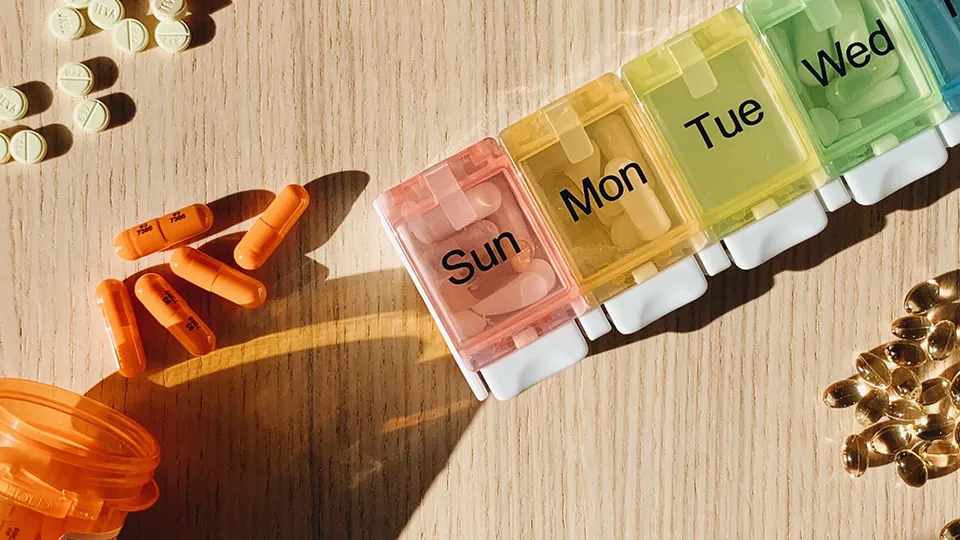 A weekly pill organizer beside open prescription bottles and tablets on a table.