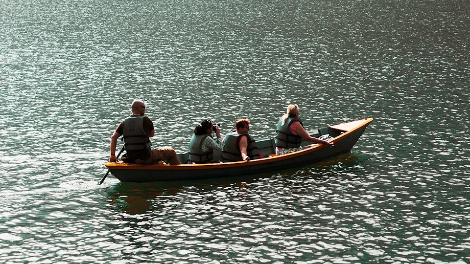 A group in life jackets out on a lake in a small boat, forested hills behind them.