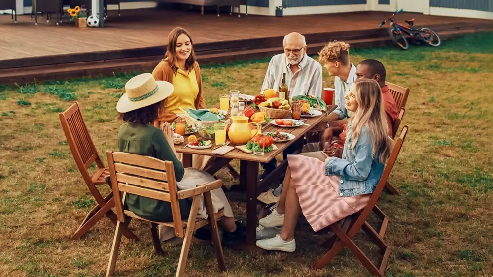 A family of three generations sharing a meal at a long table in the backyard.
