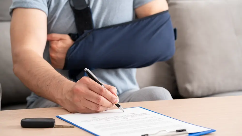 A clinician making notes on a clipboard beside a patient with a dressing taped to their arm.
