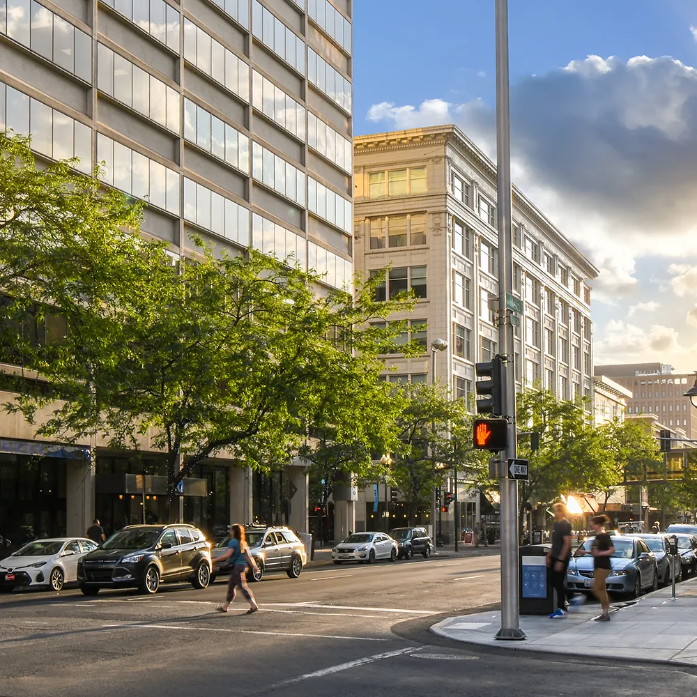 A downtown street with people crossing at the corner beside tall buildings.