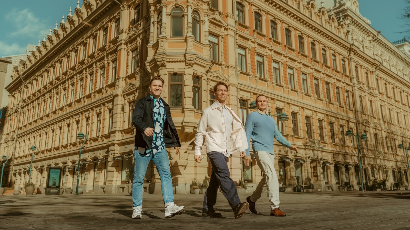Three men walking past a historic building in Helsinki