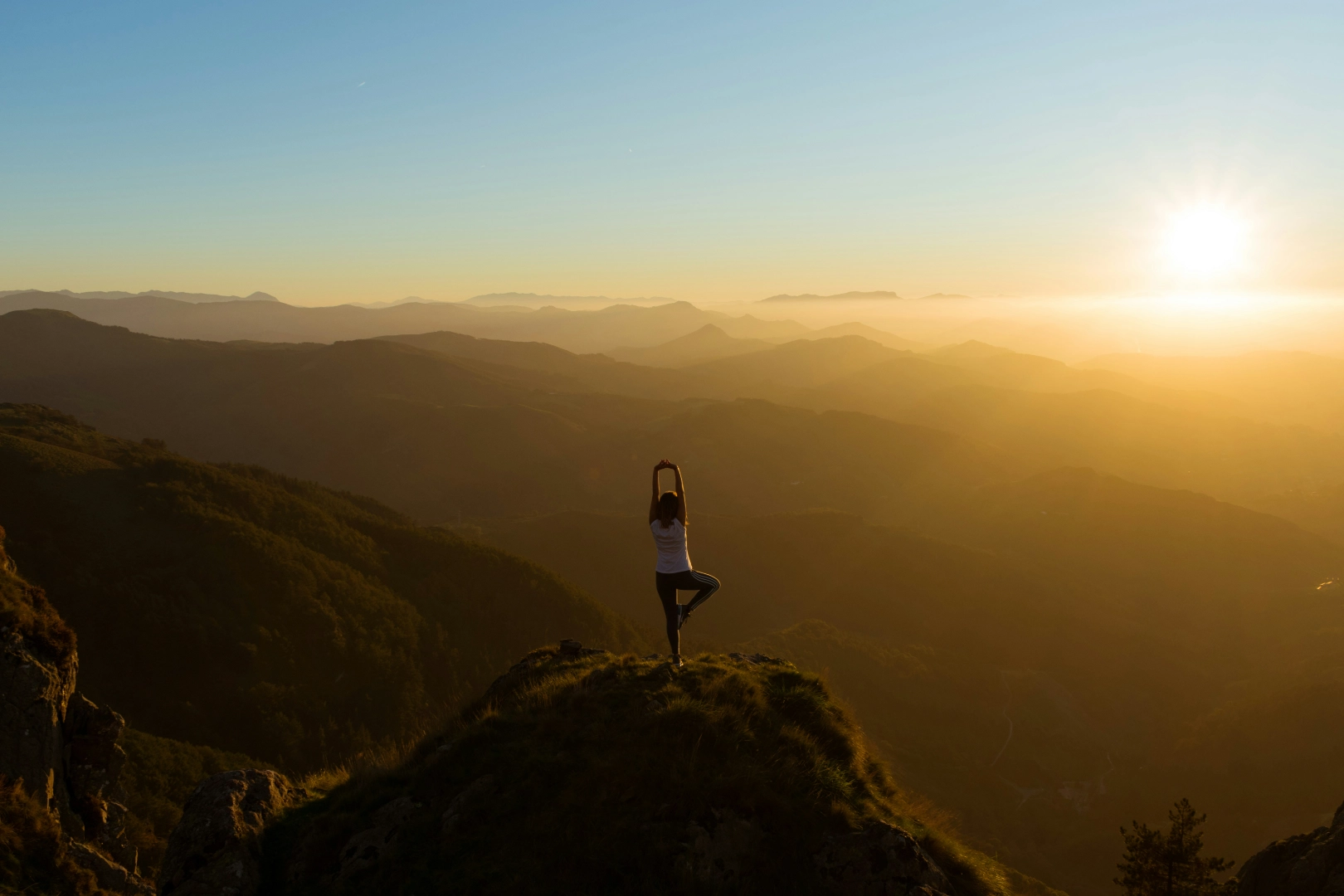 Person in a tree pose on a mountain ridge silhouetted by the setting sun