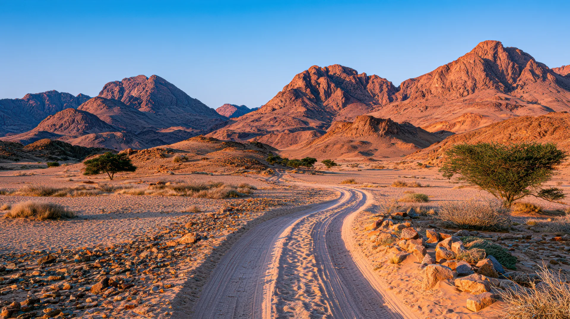 Winding dirt road through desert hills toward distant red mountains at sunset