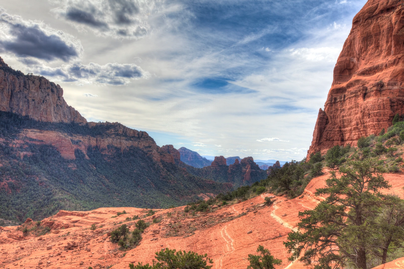 Hiker's view over a red rock canyon from a Sedona trail under dramatic clouds