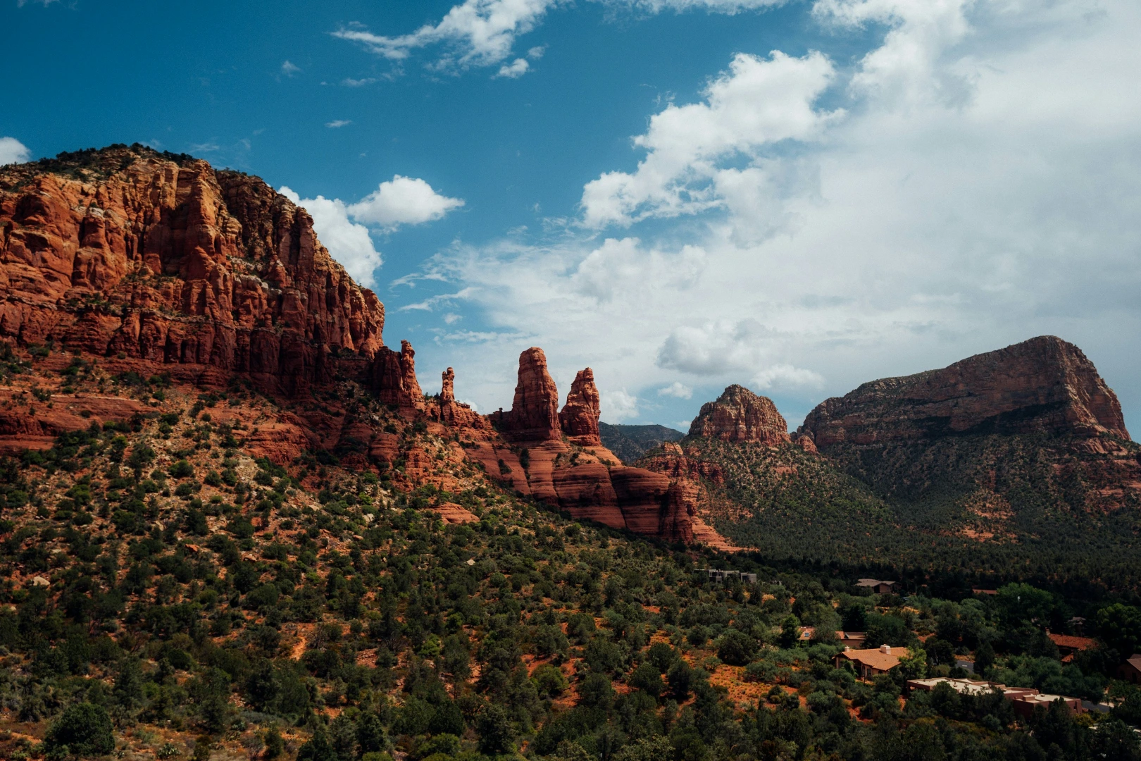 Red rock buttes and spires rising above a green juniper valley under a blue sky