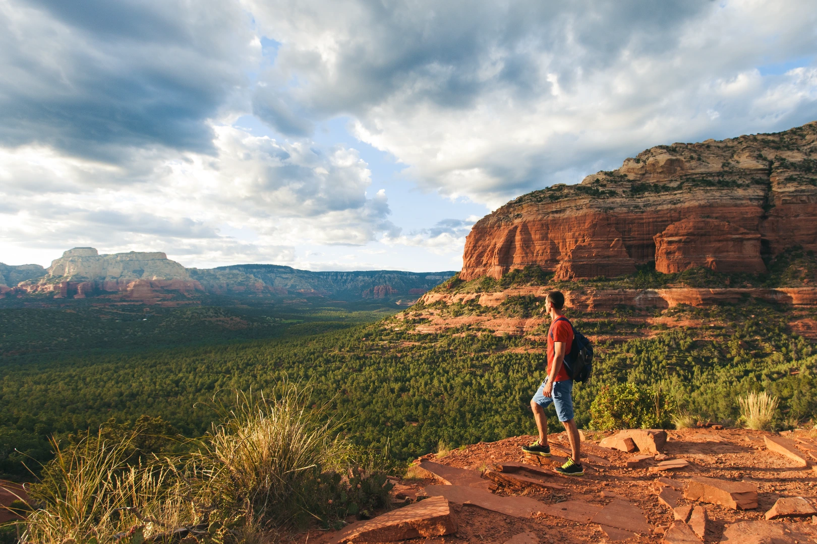 Hiker with a backpack looking out over a Sedona valley from a red rock ledge