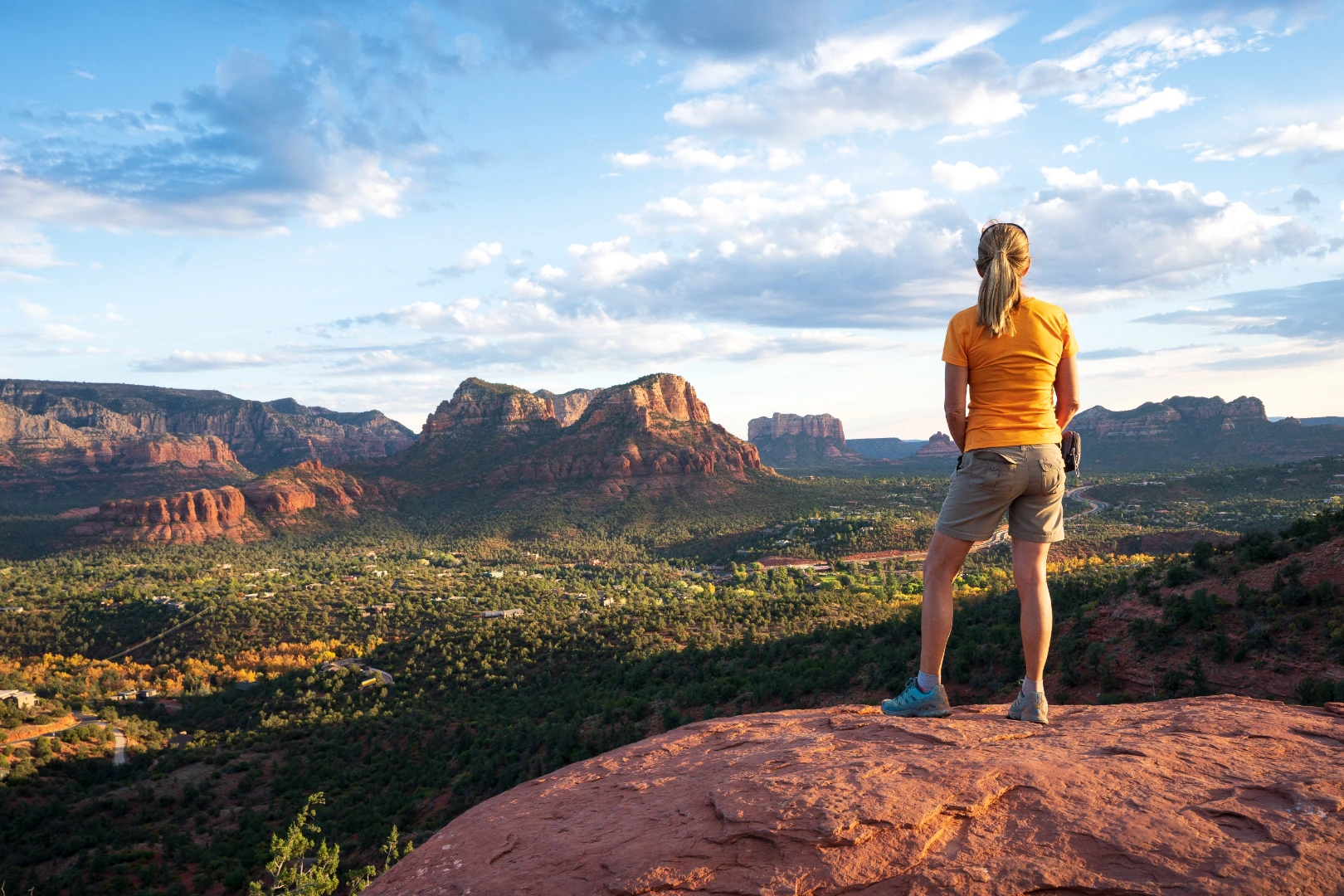 Hiker in an orange shirt looking over Sedona red rocks from a sandstone ledge