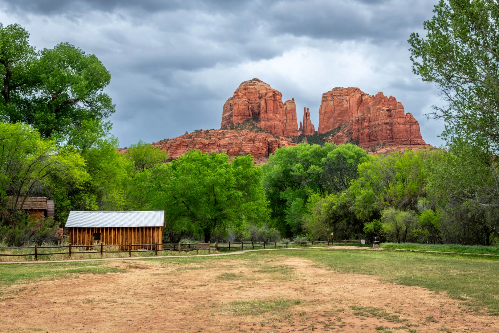 Cathedral Rock rising above green trees and a rustic barn at Red Rock Crossing