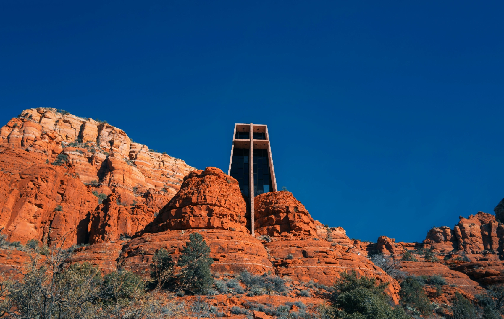 Chapel of the Holy Cross with its tall cross, built into red rock under deep blue sky