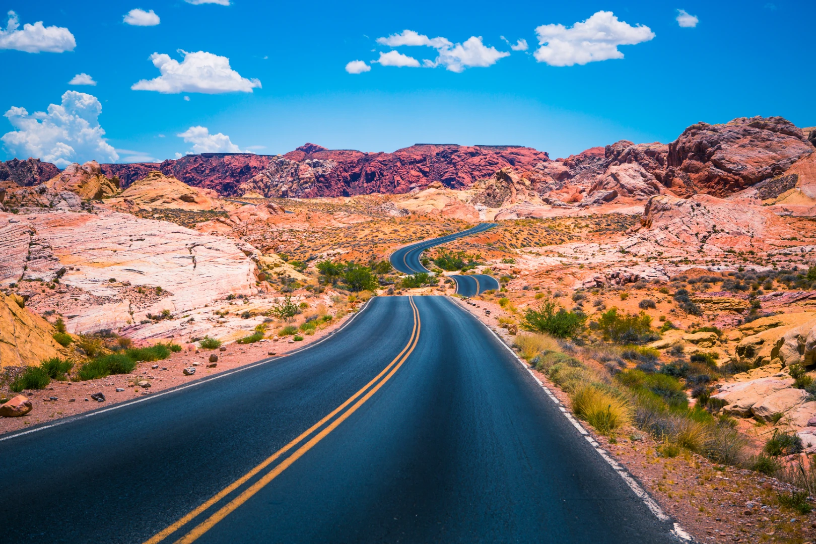 Winding two-lane road through red and white desert rock under bright blue sky