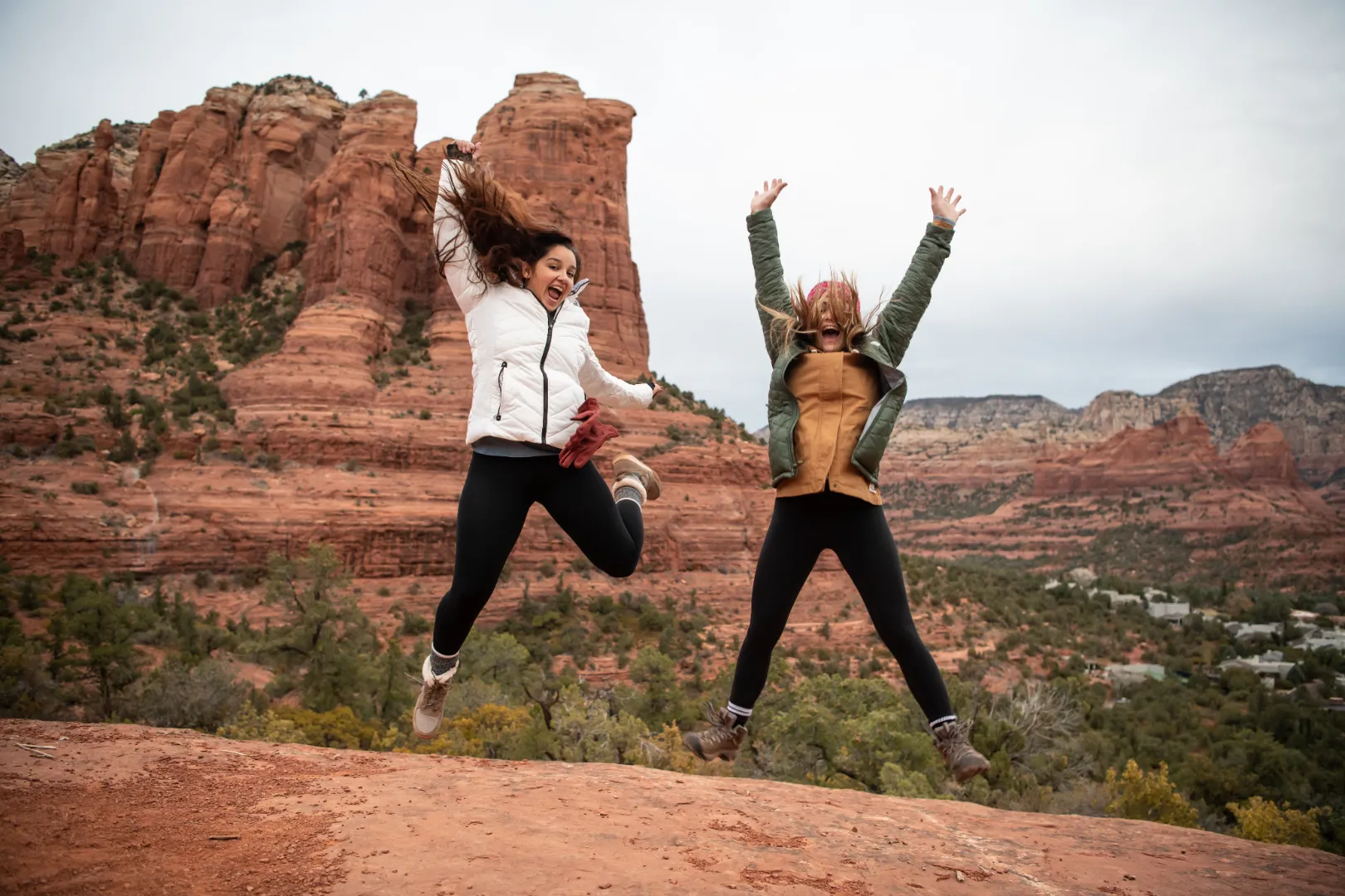 Two friends jumping joyfully on red rock above a Sedona valley