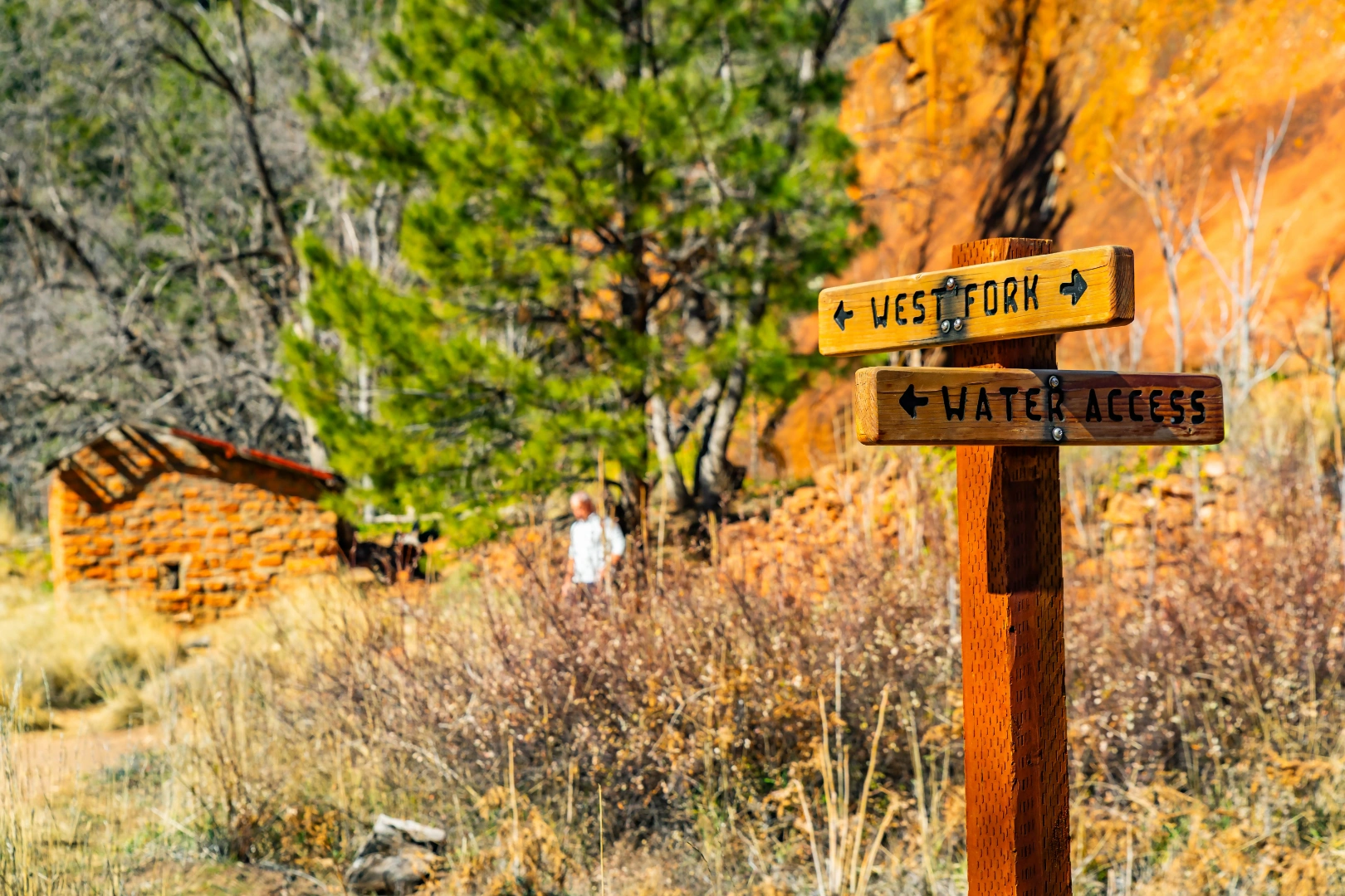 Wooden trail sign for West Fork and Water Access beside a stone cabin and autumn foliage
