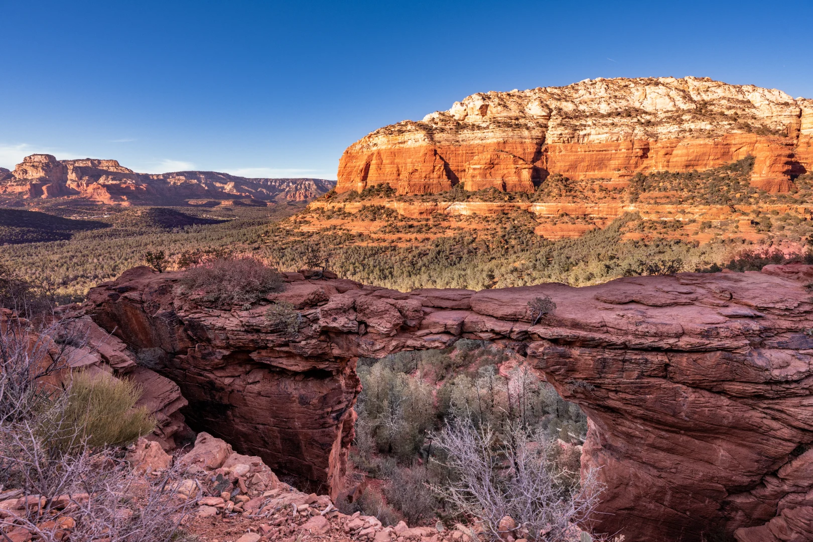 Red rock mesa and a natural sandstone arch seen from a sunlit Sedona trail overlook