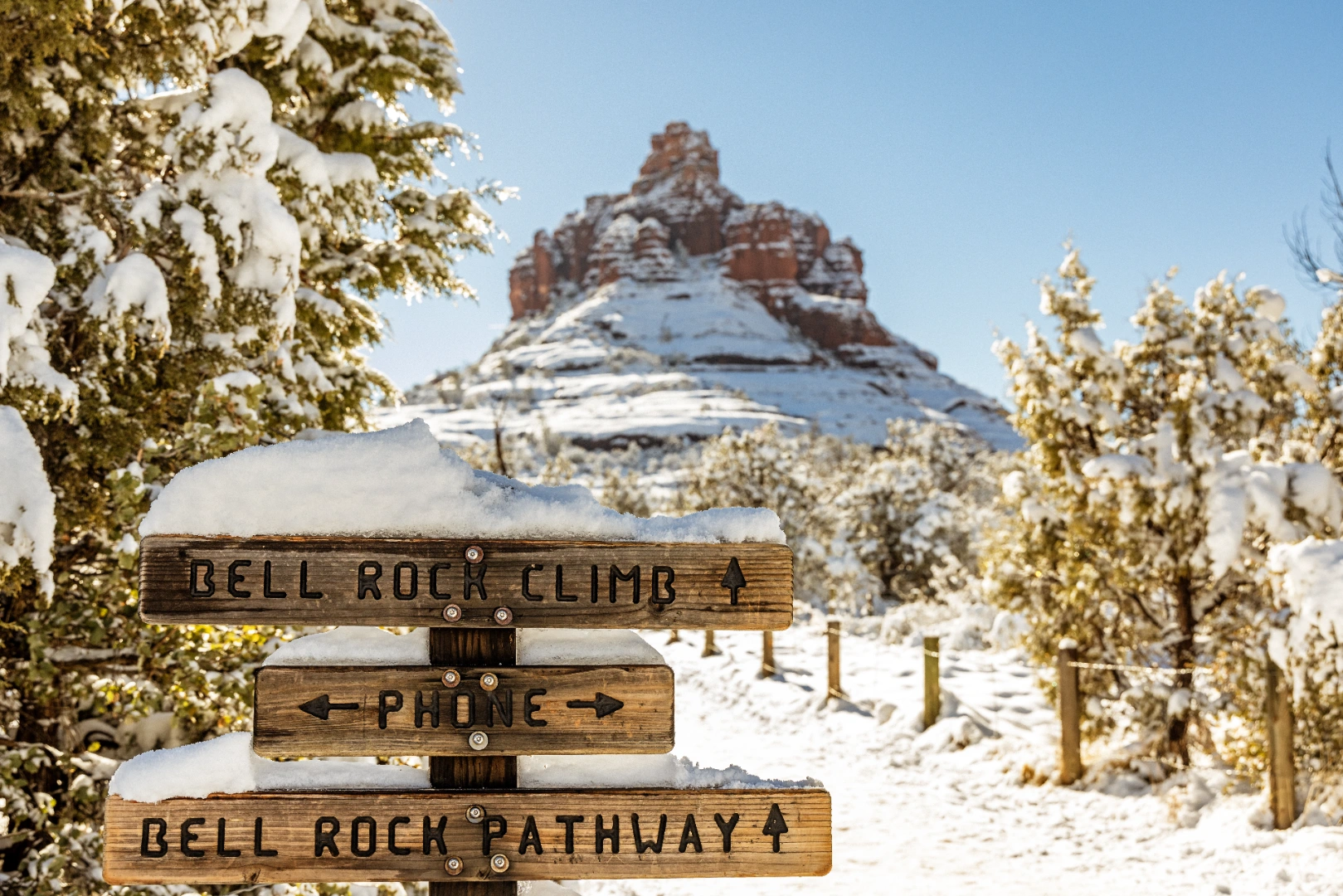Snow-covered Bell Rock Climb and Bell Rock Pathway trail signs with snowy Bell Rock behind