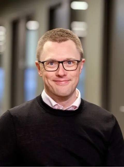 Portrait photo of a smiling man wearing glasses and a dark sweater