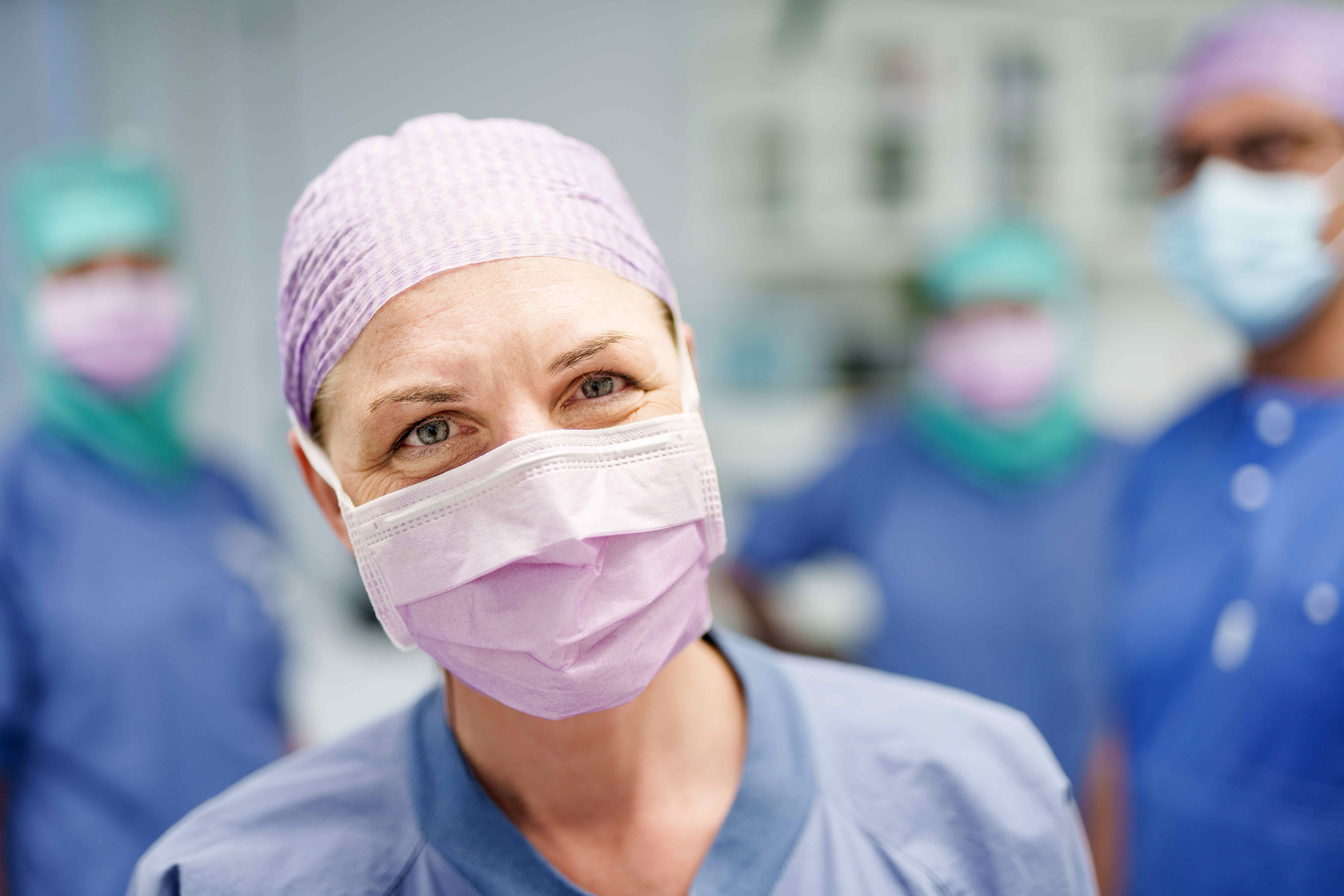 Healthcare worker in scrubs and a surgical mask in front of an Aleris sign