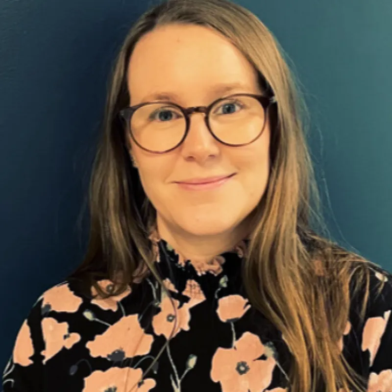 Portrait photo of Linda Edvardson, a smiling woman wearing glasses and a floral top