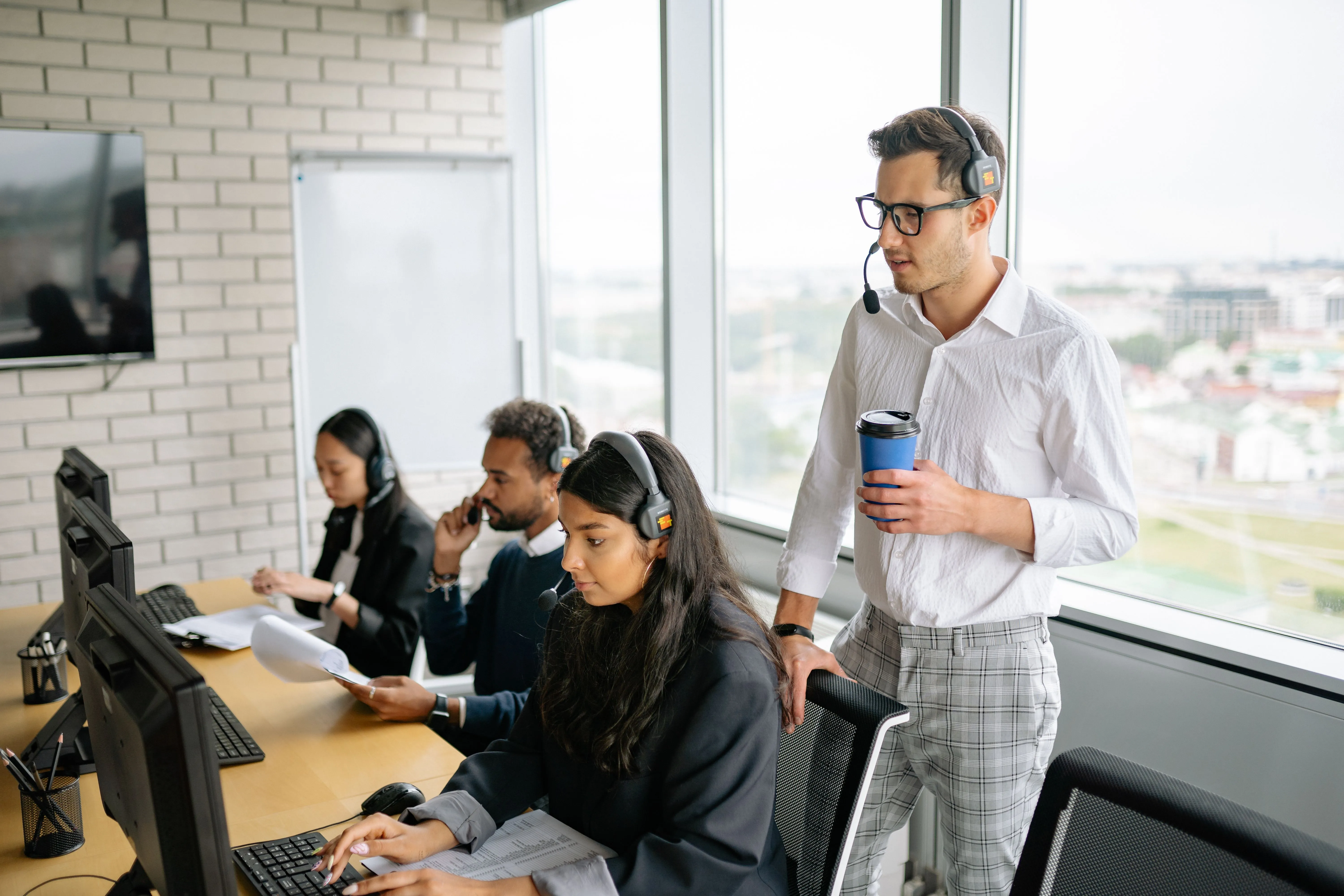 Call center agents wearing headsets at their desks with a supervisor standing nearby