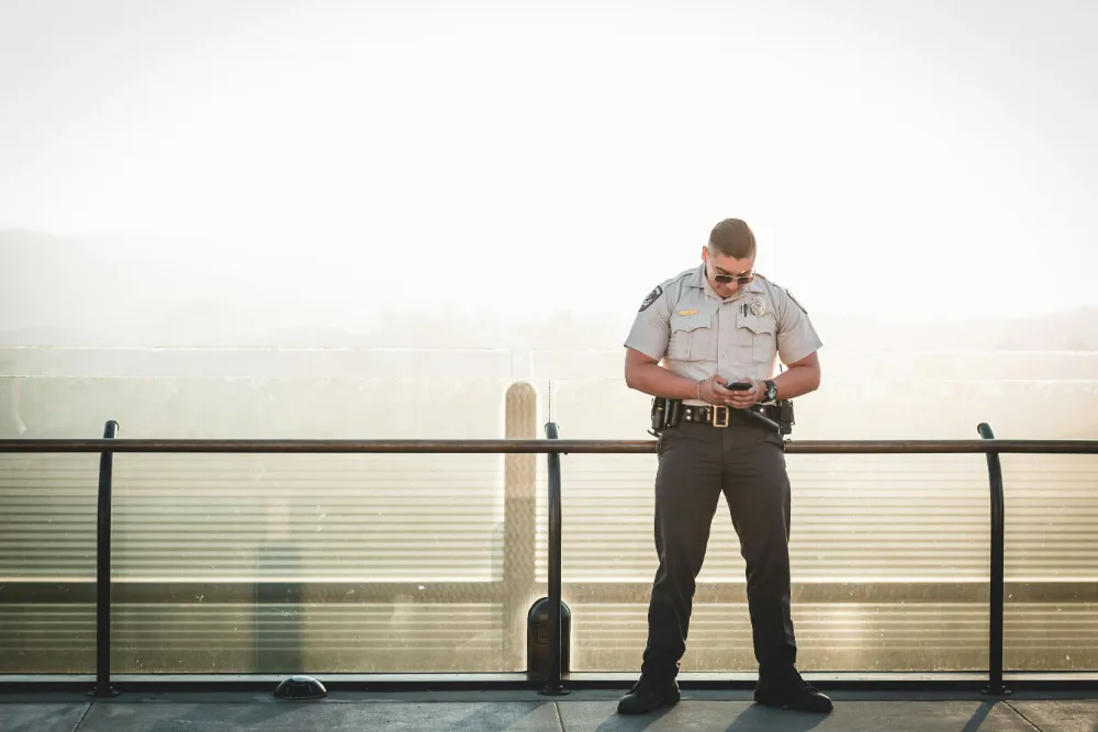 Security guard in uniform checking a phone on an outdoor walkway