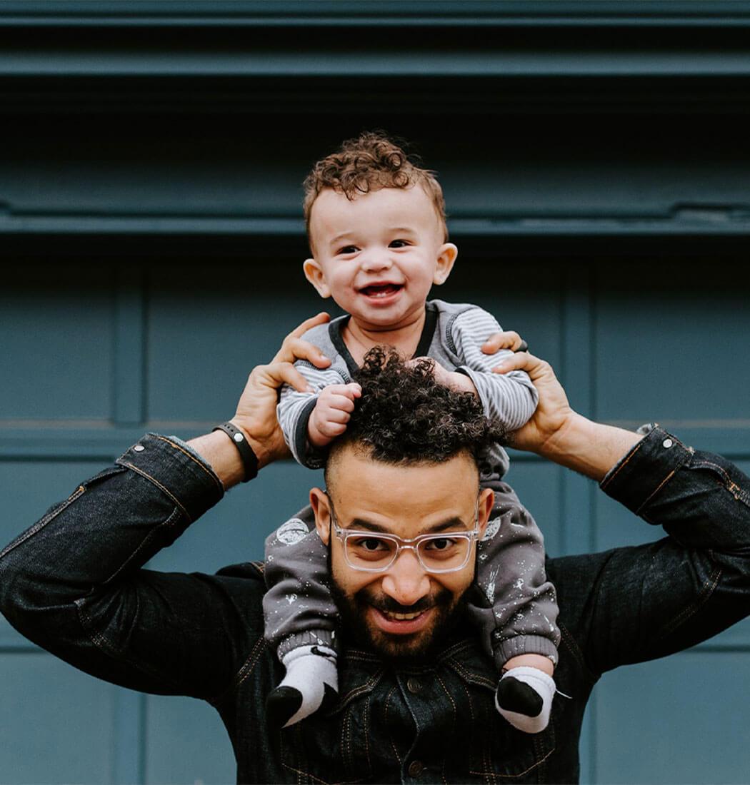 A smiling father carrying his young son on his shoulders