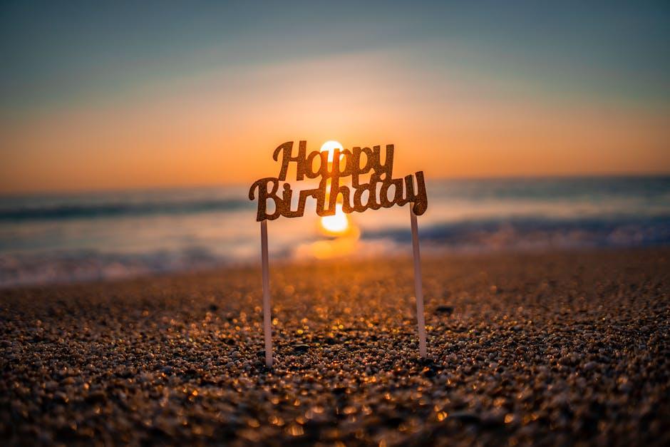 A Happy Birthday cake topper on the beach at sunset