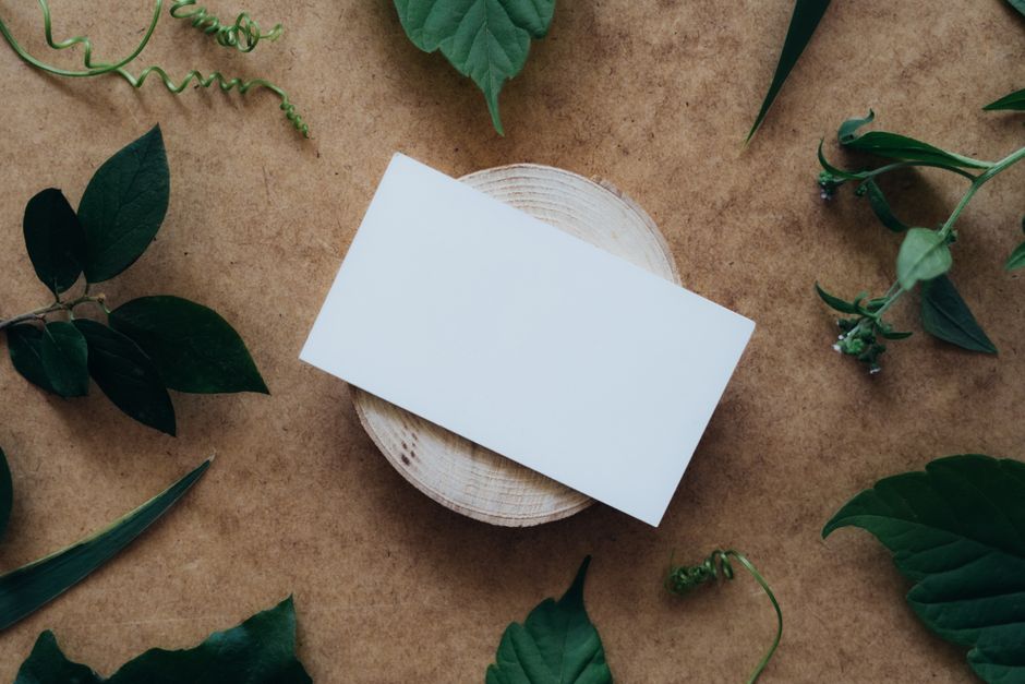 Blank card on a wooden table surrounded by green leaves