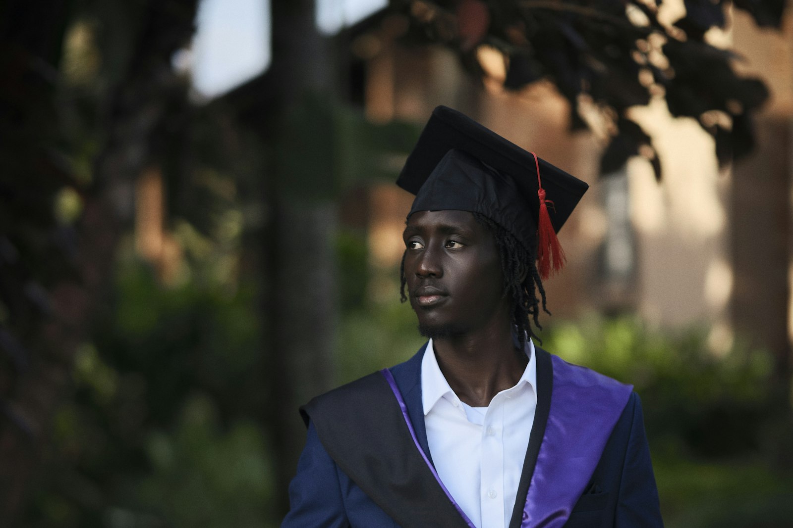 A graduate in cap and gown standing outdoors under trees