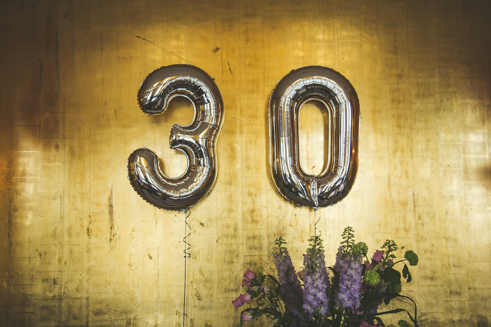 Silver number 30 balloons above a vase of purple flowers
