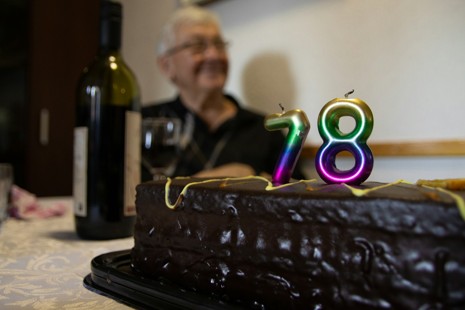 An older man smiling behind a chocolate birthday cake with number 78 candles