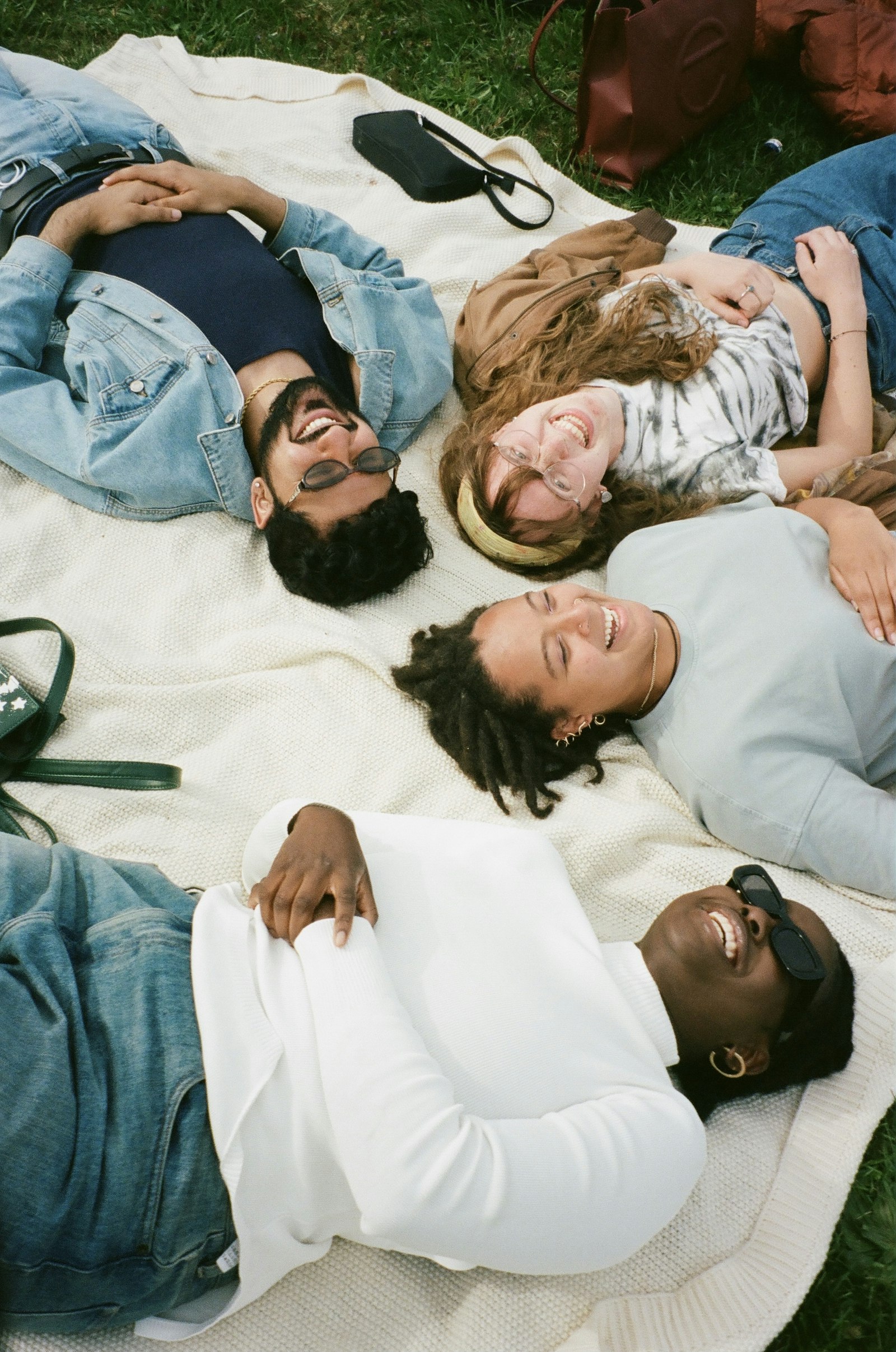 Four friends lying on a picnic blanket in the grass, laughing together