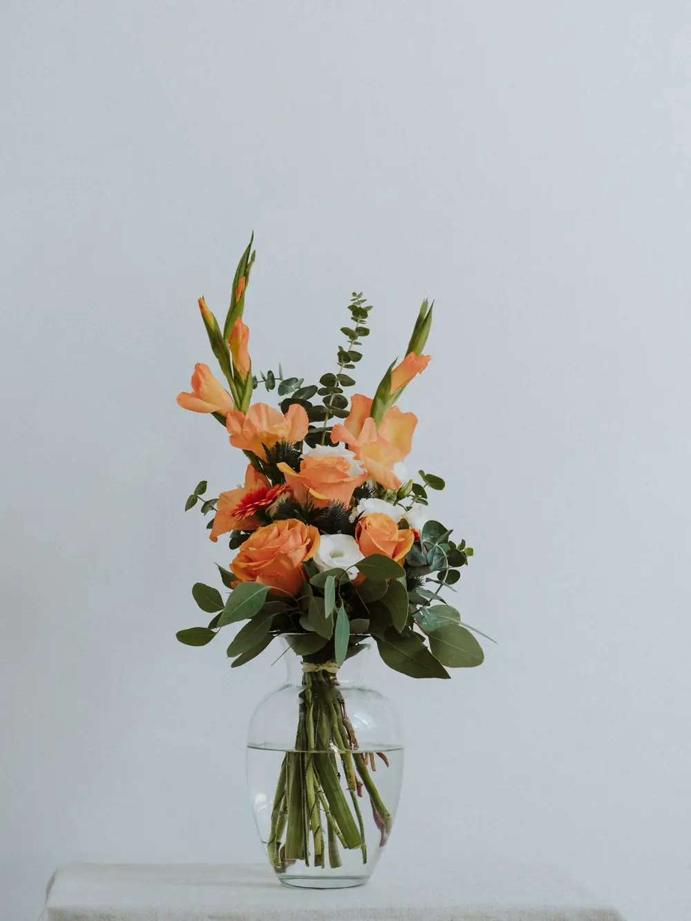 A bouquet of peach roses and gladiolus in a glass vase