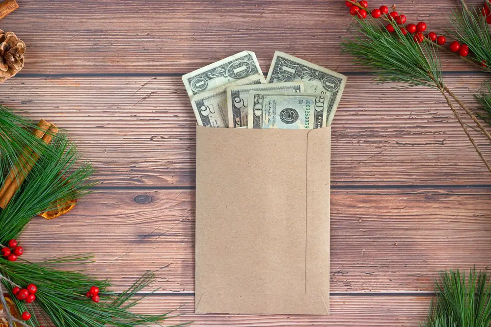 Dollar bills tucked into a kraft paper envelope on a wooden table with pine branches