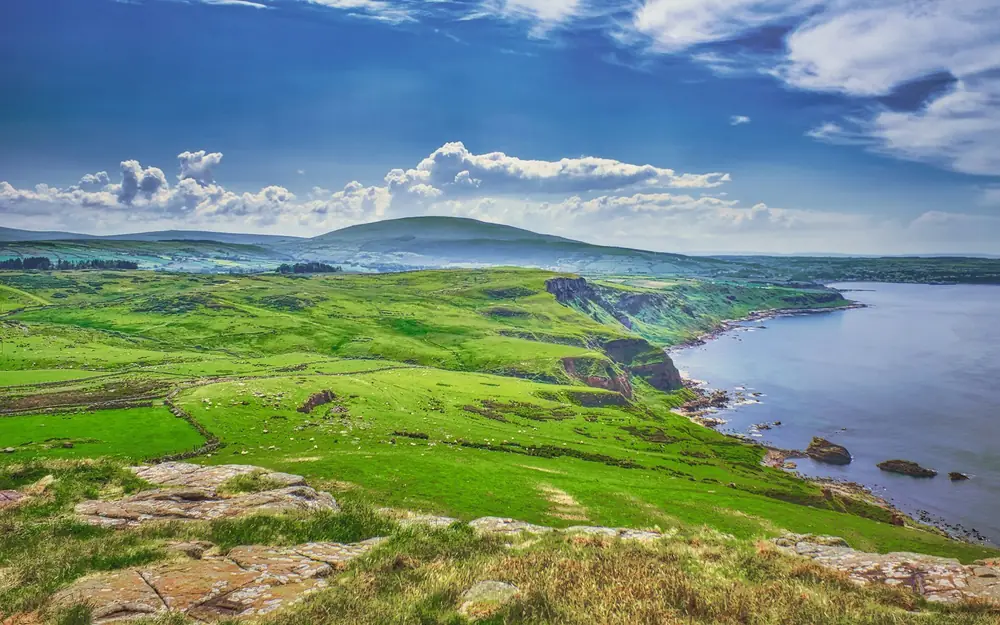Green hills and a rocky coastline under a blue sky